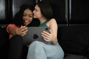dos joven mujer sentado en el cama en dormitorio y utilizando un digital tableta. foto