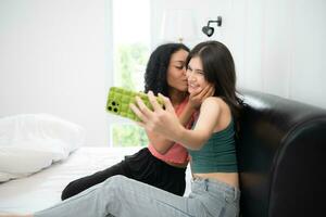 dos multiétnico mujer tomando selfie en móvil teléfono en cama a hogar foto