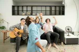 multiétnico grupo de amigos teniendo divertido jugando guitarra y canto juntos a hogar foto