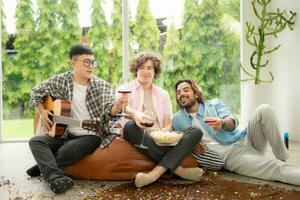 multiétnico grupo de amigos teniendo divertido jugando guitarra y canto juntos a hogar foto