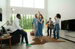 grupo de multiétnico amigos teniendo divertido a fiesta por jugando guitarra y canto juntos a hogar. foto