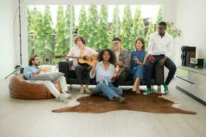 grupo de multiétnico amigos teniendo divertido a fiesta por jugando guitarra y canto juntos a hogar. foto