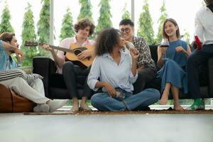 Group of multiethnic friends having fun at party by playing guitar and singing together at home. photo