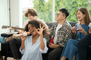 Group of multiethnic friends having fun at party by playing guitar and singing together at home. photo