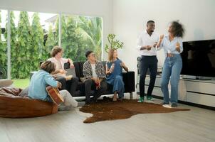 Group of multiethnic friends having fun at party by playing guitar, singing and dance together at home. photo