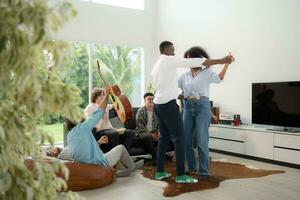 Group of multiethnic friends having fun at party by playing guitar, singing and dance together at home. photo