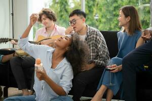 Group of multiethnic friends having fun at party by playing guitar and singing together at home. photo