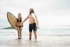 Couple of surfers holding hands and looking at each other on beach photo