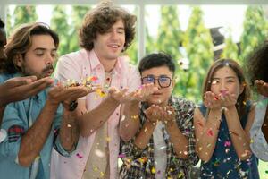 Group of multiethnic friends having fun at party playing fun blowing colorful paper photo