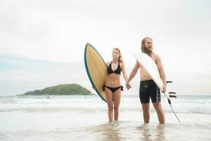 Pareja de surfistas participación manos y mirando a cada otro en playa foto