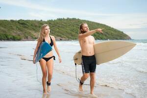 joven hombre y mujer participación tablas de surf Listo a caminar dentro el mar a navegar. foto