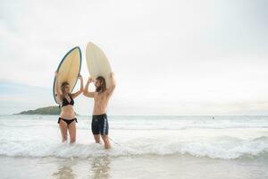 Young man and woman holding surfboards on their heads and walk into the sea to surf photo