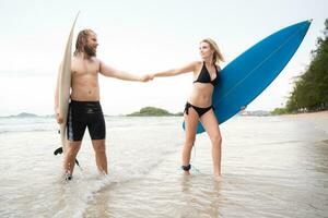 Couple of surfers holding hands and looking at each other on beach photo