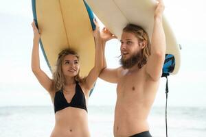 Young man and woman holding surfboards on their heads and walk into the sea to surf photo