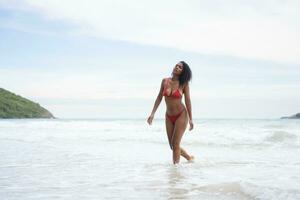 Portrait of happy young woman in red bikini walking on the beach. photo