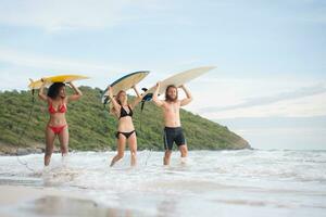 Rear view of two women and young man holding surfboards on their heads. and walk into the sea to surf photo