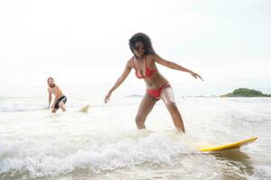 Couple surfing on the beach having fun and balancing on the surfboard photo