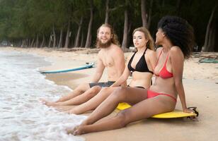 Group of multiracial friends sitting on surfboards on sandy beach photo