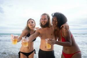 multiétnico grupo de amigos teniendo divertido en el playa, Bebiendo cerveza y teniendo divertido foto