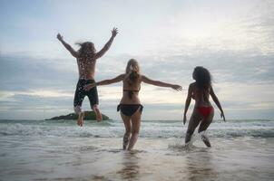 grupo de amigos teniendo divertido en el playa a el puesta de sol tiempo. foto