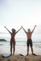 Back view of man and woman in swimsuit standing with surfboard on the beach photo