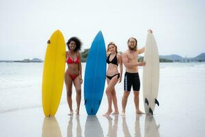 grupo de amigos en trajes de baño posando con tablas de surf en el playa. foto