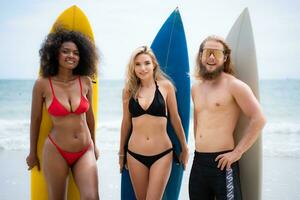 grupo de amigos en trajes de baño posando con tablas de surf en el playa. foto