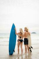 Rear view of young man and woman in swimsuits with surfboards on the beach. photo