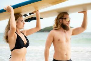 Young man and woman holding surfboards on their heads and walk into the sea to surf photo