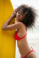 Portrait of smiling young woman in bikini with surfboard at beach photo