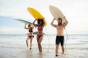 Rear view of two women and young man holding surfboards on their heads and walk into the sea to surf photo