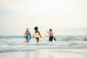 Two women and young man holding surfboards ready to walk into the sea to surf. photo