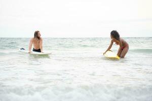 Young men teaching surfing with a surfboard with young women in red swimsuits photo