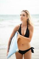 retrato de sonriente joven mujer en pie con tabla de surf a el playa foto