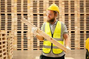 retrato de joven masculino carpintero trabajando en un carpintería fábrica, él es vistiendo un la seguridad casco y anteojos, comprobación el de madera tablones viniendo fuera de el madera amoladora. foto