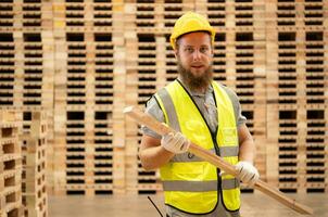 Portrait of young male carpenter working in a woodworking factory, He is wearing a safety helmet and glasses, Checking the wooden planks coming out of the wood grinder. photo
