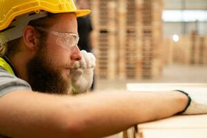 A guy carpenter in a hardhat and glasses inspects a completed work item at a timber industry. photo