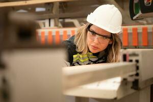 Young woman worker work in a woodworking factory, Working with wood sawing and cutting machines to produce wooden sheets for making pallets photo