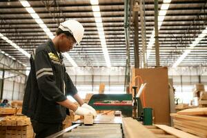 Young man worker work in a woodworking factory, Working with wood sawing and cutting machines to produce wooden sheets for making pallets photo