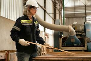 A carpenter works in a carpentry workshop. She collects the wood that passes through the wood angle grinder. photo