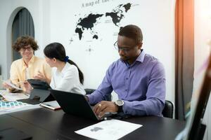 Multiethnic team of architects and designers are meeting to brainstorm design an application smartphone on a bright modern office working on a laptop. photo