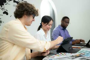 Multiethnic team of architects and designers are meeting to brainstorm design an application smartphone on a bright modern office working on a laptop. photo