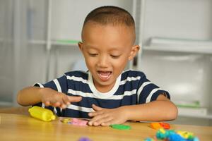 Boy making plasticine to promote development on the table in the house. photo