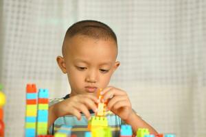 asiático chico jugando con educativo juguetes allí son muchos hermosa colores en el mesa en el casa. foto