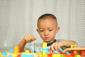 asiático chico jugando con educativo juguetes allí son muchos hermosa colores en el mesa en el casa. foto