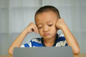 un chico es aburrido porque él mira a el computadora para un largo tiempo. foto