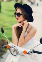 Close up fashion  portrait of  pretty young blonde woman in white tulle skirt and black heels sitting on  vintage scooter. Spring sunny city. photo