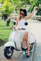 pretty young blonde woman in white tulle skirt and black heels sitting on  vintage scooter. Spring sunny city. photo