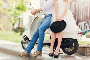 Fashionable couple posing on the street, siting on scooter , wearing stylish casual clothes, black hat and  white tulle skirt.Vintage  soft  colors.Sunlight. Fashion details. photo