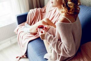 Close up indoor portrait of graceful blonde woman enjoying smell of cappuccino  , dreaming and looking into the window.  Wearing pink knitted sweater. photo